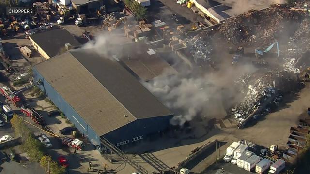 An aerial view of a warehouse with smoke pouring out of the roof. 