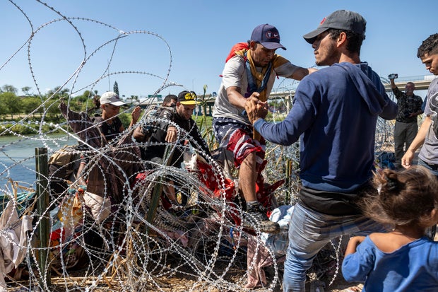 Immigrants cross over razor wire after crossing from Mexico into the United States on Sept. 28, 2023, in Eagle Pass, Texas.