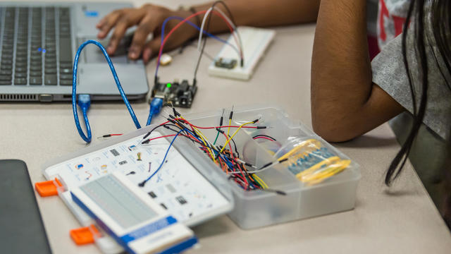 Female high school student using a control board and circuitry kit with a computer for a STEM project in a  computer science class 