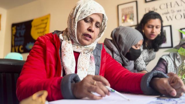 South Asian women sit around a dining room table working on English language practice sheets. 