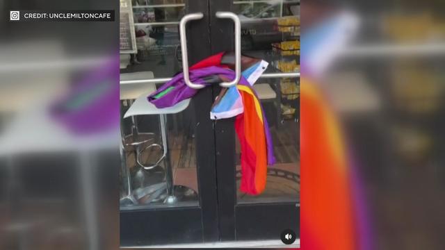 A Pride flag wrapped around exterior door handles on the front door of a cafe. 