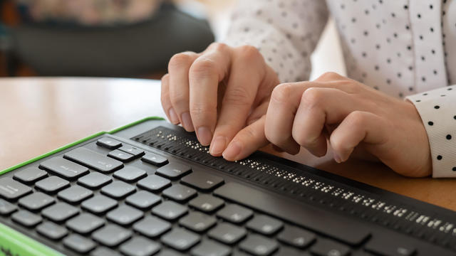 A blind woman uses a computer with a Braille display and a computer keyboard. Inclusive device. 