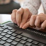 A blind woman uses a computer with a Braille display and a computer keyboard. Inclusive device. 