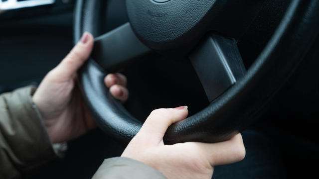 Detail of a woman's hands gripping the steering wheel while driving a car. 