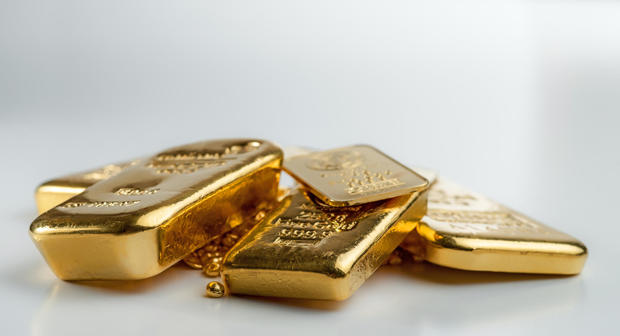 Several different gold bars lie on a pile of gold pellets 