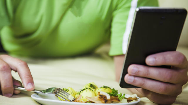 Man eating dinner sitting  on bed & looking up social media on mobile phone. 