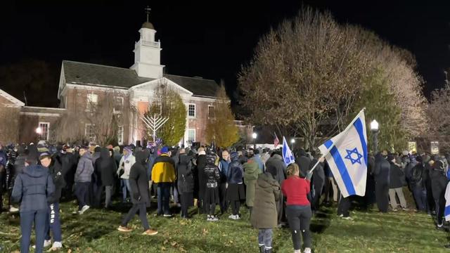 Hundreds of people, some holding Israeli flags, stand outside the Teaneck Municipal Building. 