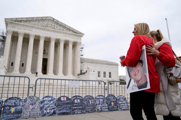 Jen Trejo holds a photo of her son Christopher as she is comforted outside the Supreme Court on Monday, Dec. 4, 2023, in Washington.