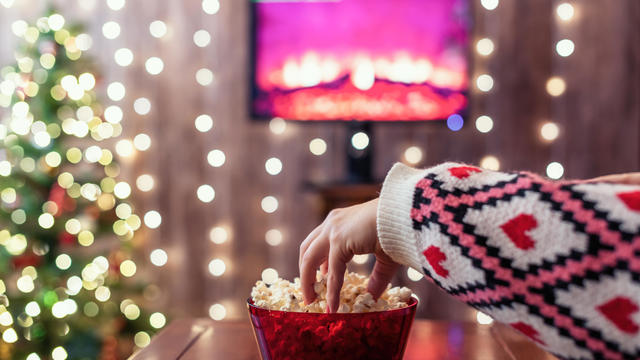 Christmas eve. Alone woman watching tv and eating popcorn. Home cinema. Cropped, close up 