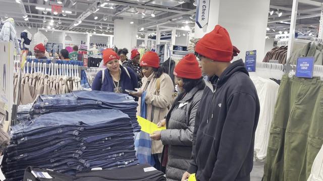Four volunteers in red winter hats stand in front of a table of jeans inside an Old Navy. 