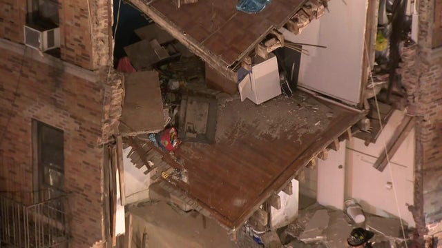 The corner of an apartment building -- the exterior walls have collapsed, exposing the apartments inside.