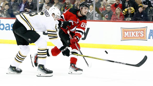 Jack Hughes #86 of the New Jersey Devils takes a shot on goal as Mason Lohrei #6 of the Boston Bruins defends during overtime at Prudential Center on December 13, 2023 in Newark, New Jersey. The Devils won 2-0 in overtime.