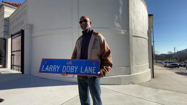 Larry Doby Jr. holds a street sign reading "Larry Doby Lane" outside Hinchliffe Stadium. 