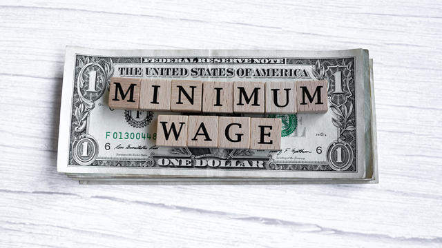 Minimum wage word written on wood block with American Dollar-bills. Directly above. 