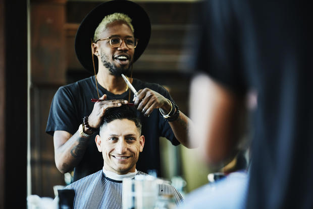 Smiling barber in discussion with client while cutting hair in barber shop 