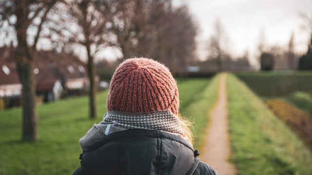 Woman walking on a narrow path dressed in warm clothes from behind 