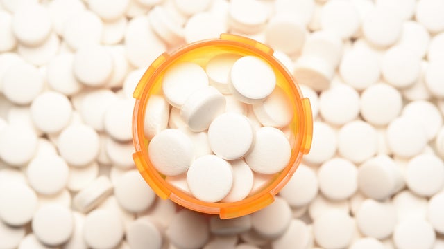 Prescription bottled filled with pills surrounded by more of the same tablets