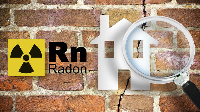 The danger of radon gas in our homes - concept with periodic table of the elements, radioactive warning symbol and home silhouette seen through a magnifying glass against a cracked brick wal 