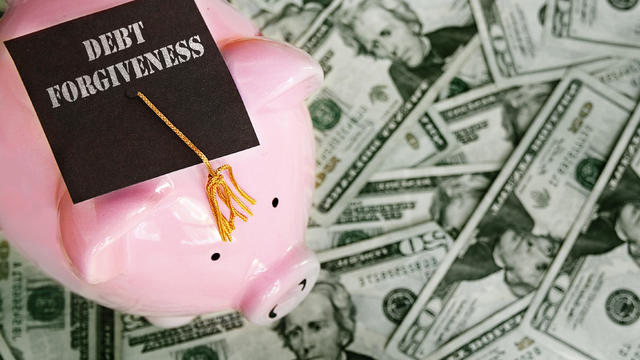 Piggy bank with Debt Forgiveness graduation cap on cash 
