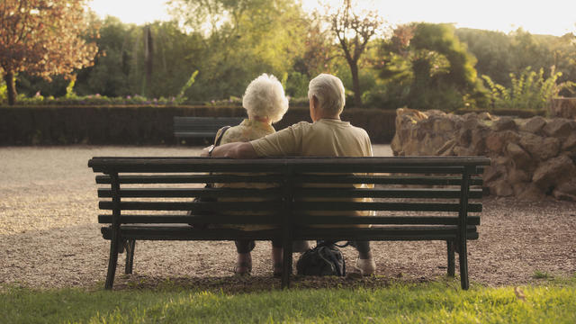 Senior couple sitting on bench in park, rear view 