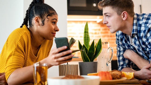 Young couple indoors at home leaning on table, using smartphone 