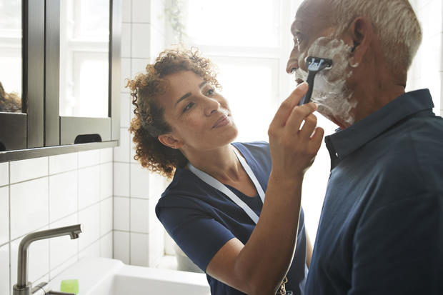 Healthcare worker assisting senior man in shaving 