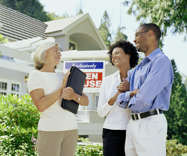 Mature woman standing with couple in front of Open House sign 