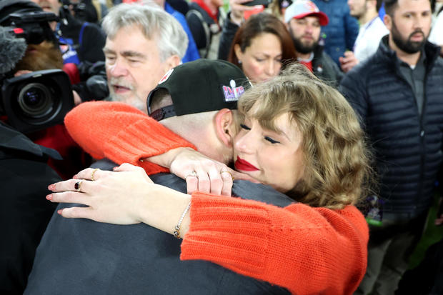 Taylor Swift, wearing a tennis bracelet with the letters TNT, hugs Travis Kelce on the field after the AFC Championship game. 