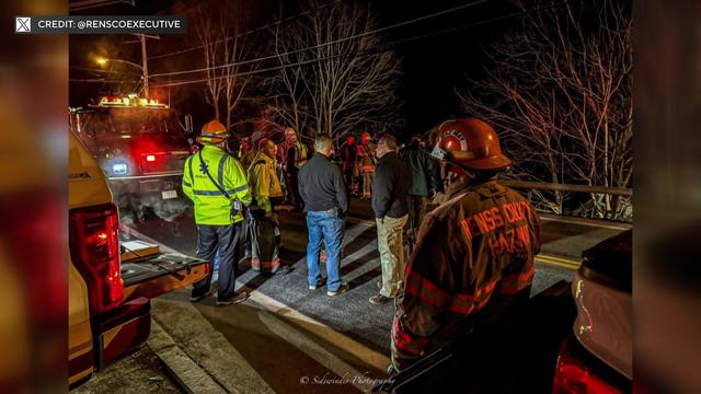 Emergency responders stand on a street at night. 