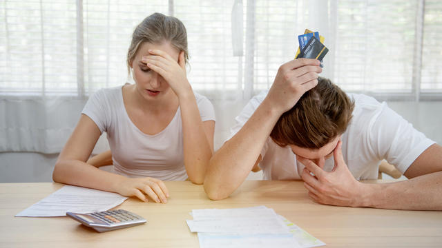 Young caucasian couple hand holding credit card and debt bill on table in home,men and women have overdue financial foreclosure problem sit in room with serious and unhappy payment. 