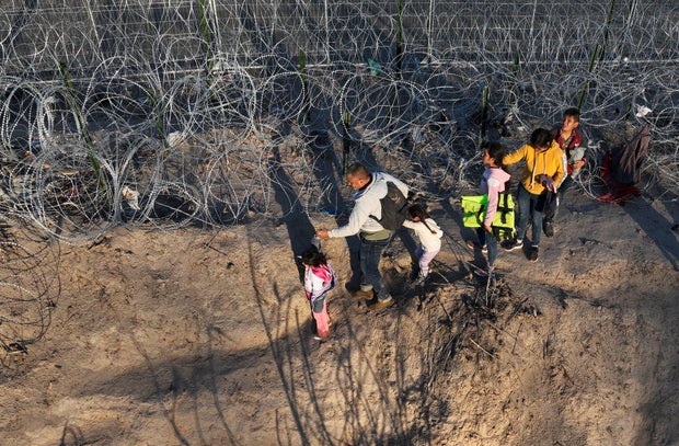 An aerial view shows migrants walking next to razor wire after crossing the Rio Grande to seek asylum at sunset in Eagle Pass, Texas, on Feb. 4, 2024.