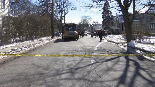 Crime scene tape blocks off a street as investigators surround a school bus. 