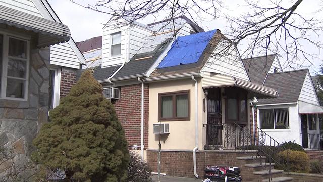 A home in Queens with a blue tarp over part of the roof and construction work being done over other parts of the roof. 
