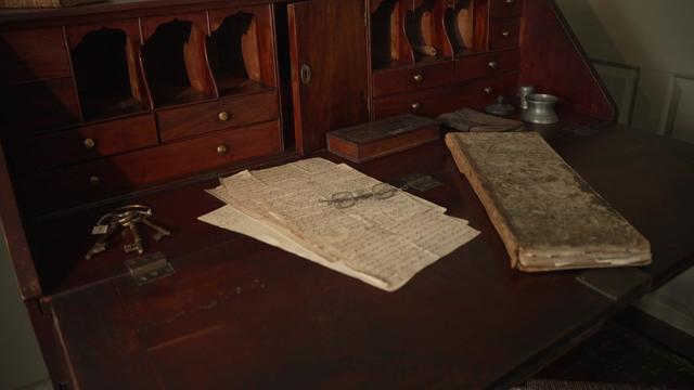 18th century books, papers and other artifacts sit on a desk. 