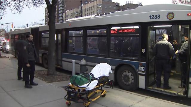 An MTA bus parked on the side of a Bronx street. NYPD officers stand outside and inside the bus and a stretcher sits on the sidewalk. 