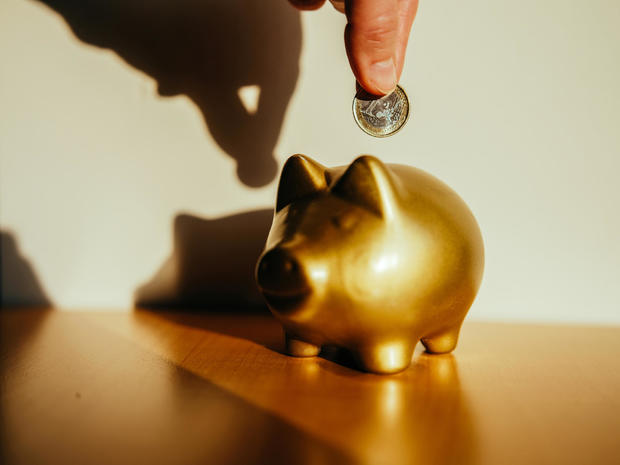 Hand putting a coin in a golden piggy bank. 