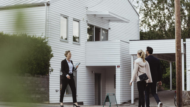 Smiling real estate professional talking to couple outside new house 