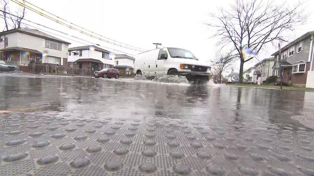 Rain water partially floods a Queens street as a white van drives through. 