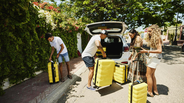 Wide shot of family loading rental car with luggage while on vacation 