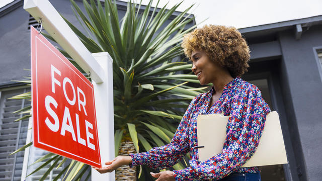 Mature real estate agent adjusting for sale sign in front of home 