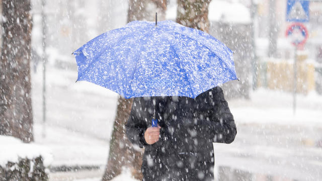 Man with umbrella under snow on city street 