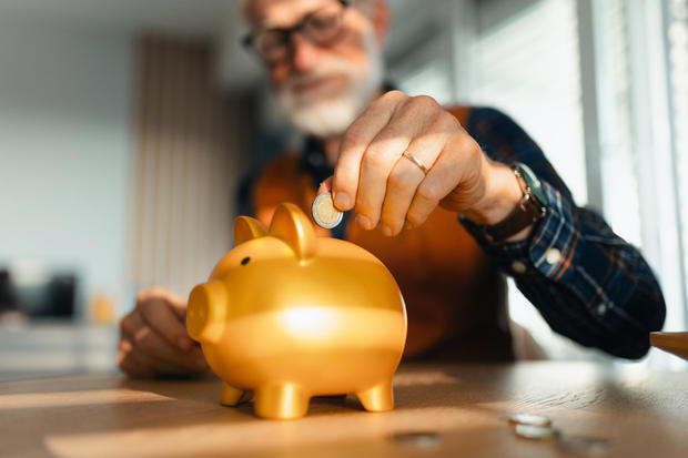 Senior man putting coins, money into a piggy bank. Saving Money after retirement, preparing for retirement. Financial education and financial literacy for seniors. 