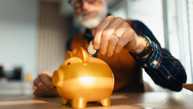 Senior man putting coins, money into a piggy bank. Saving Money after retirement, preparing for retirement. Financial education and financial literacy for seniors. 
