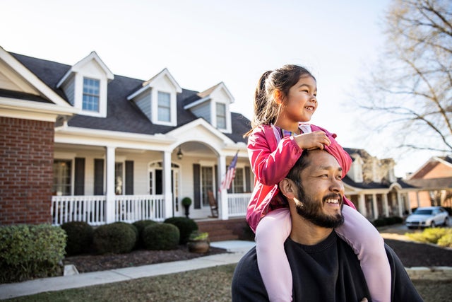 Daughter on father's shoulders in front of suburban home