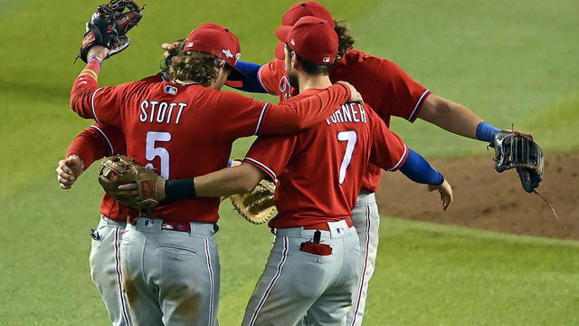 Bryson Stott and Trea Turner and other members of the Philadelphia Phillies hug on the field after a win in 2023. 