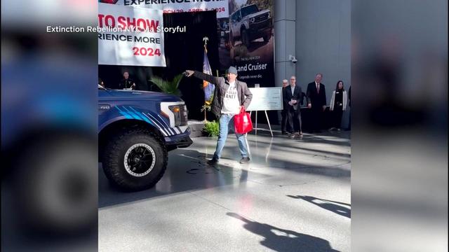 A man pours what appears to be oil on an electric vehicle at the New York International Auto Show. 