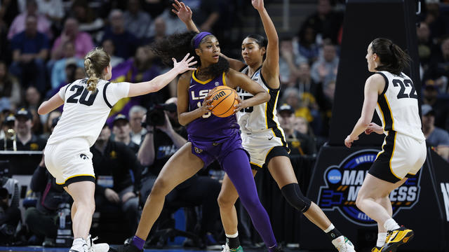 Angel Reese of LSU holds the basketball, surrounded by three Iowa players on the court 