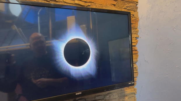 A TV screen showing a photo of a solar eclipse, where the moon is blocking the sun 