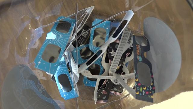 Multiple pairs of solar eclipse glasses in a clear bowl on a desk. 