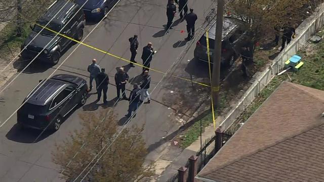 An aerial view of police officers standing on a residential street near crime scene tape. 